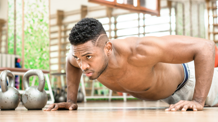 A shirtless person with a fade concentrates while they perform a push-up.