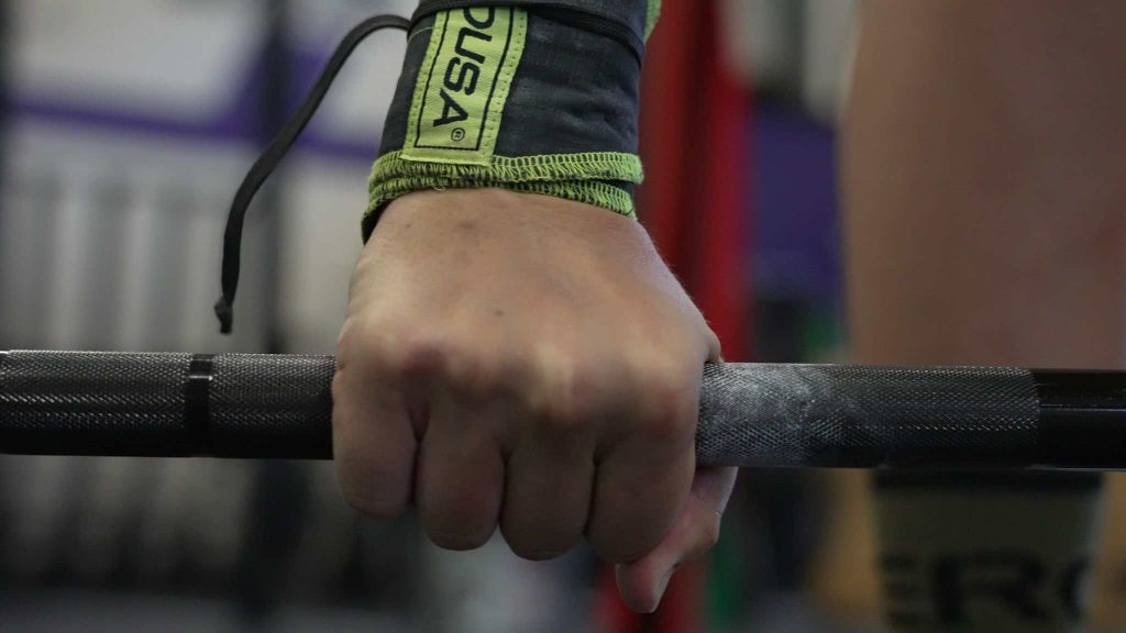a woman's hand gripping a barbell in preparation for a lift