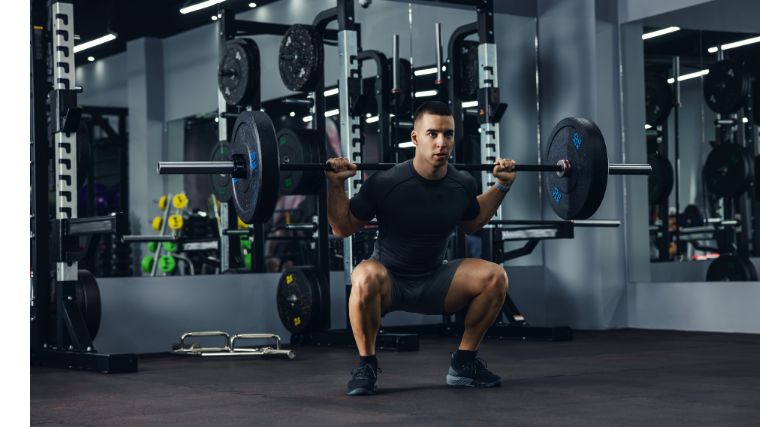 person wearing a black t-shirt and shorts squats with a loaded barbell on their back.