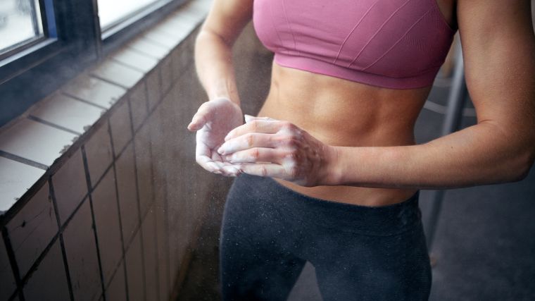 Person wearing a pink sports bra applying lifting chalk to their hands.