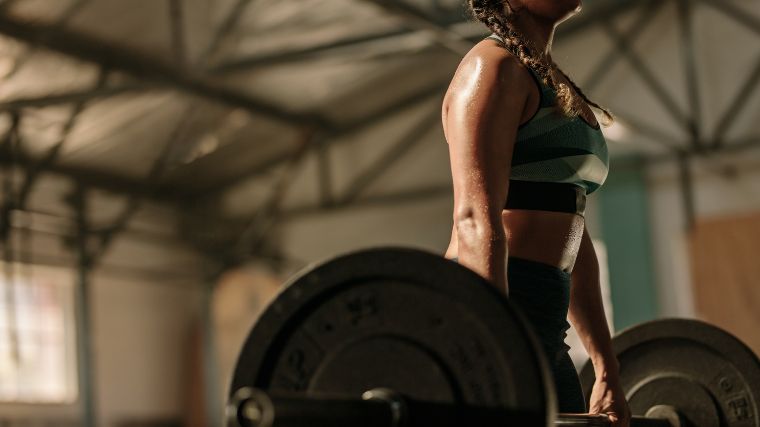 Person in camo sports bra lifting a barbell off of the floor.