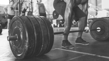 Man in black shorts gripping a loaded barbell resting on the floor with both hands