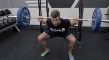 Person wearing a black t-shirt and black shorts squatting with a barbell draped across their back