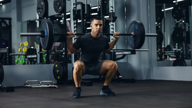 person wearing a black t-shirt and shorts squats with a loaded barbell on their back.
