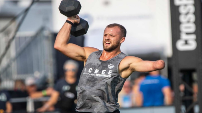 Casey Acree, an athlete in the CrossFit Upper Extremities Men's Division, hefts a dumbbell overhead.