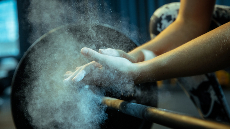 A close up image shows a person clapping their hands with chalk just above a loaded barbell.