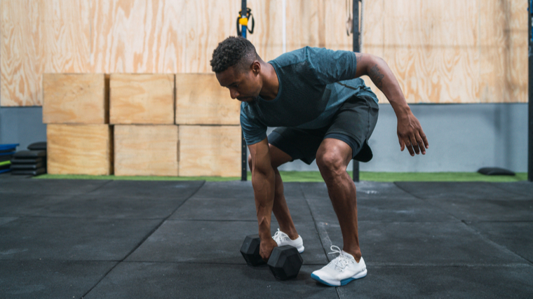 A person wearing a blue-grey t-shirt prepares to pick up a dumbbell for a snatch.