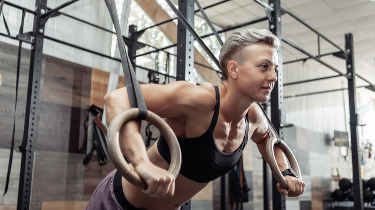 A person with short hair wears a sports bra while performing ring push-ups.