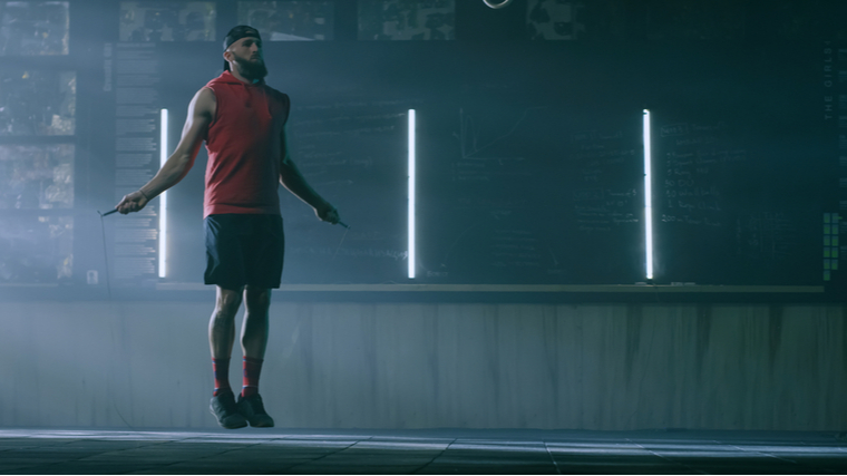 A person wears a red shirt and black shorts while performing double unders.