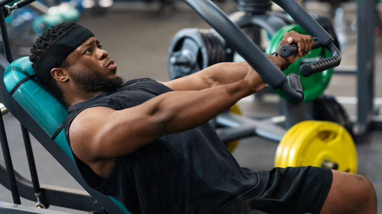 A person wears a headband and tank top while performing an incline bench press machine.