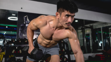 A shirtless person with a mustache performs a single-arm dumbbell row.