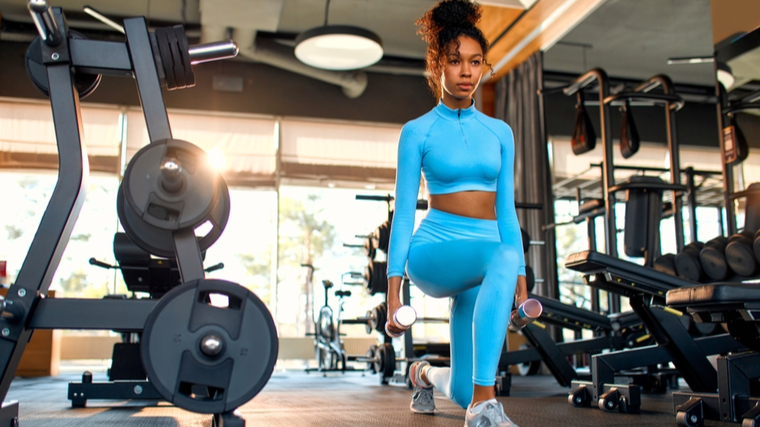 A person wearing a bright, light blue training outfit performs walking lunges with dumbbells.