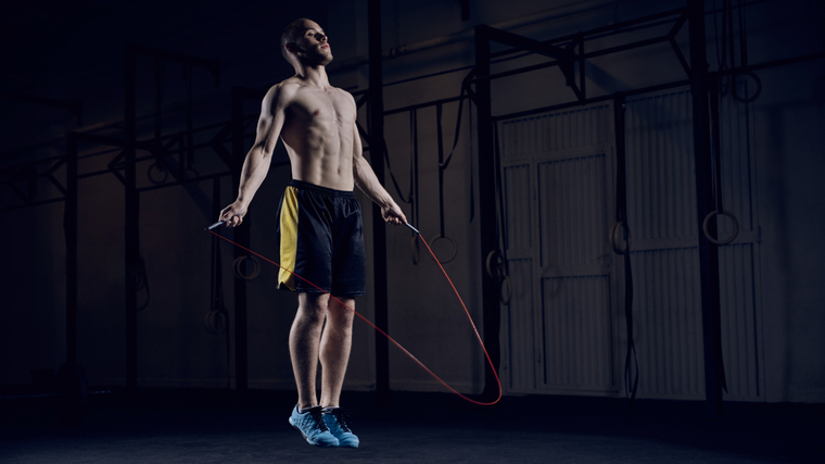 A shirtless person jumps rope in a darkly-lit gym.