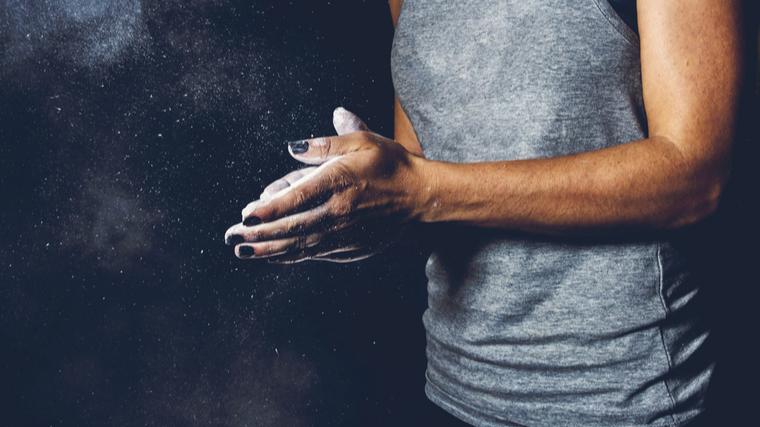 A person wearing black nail polish claps chalk onto their hands.