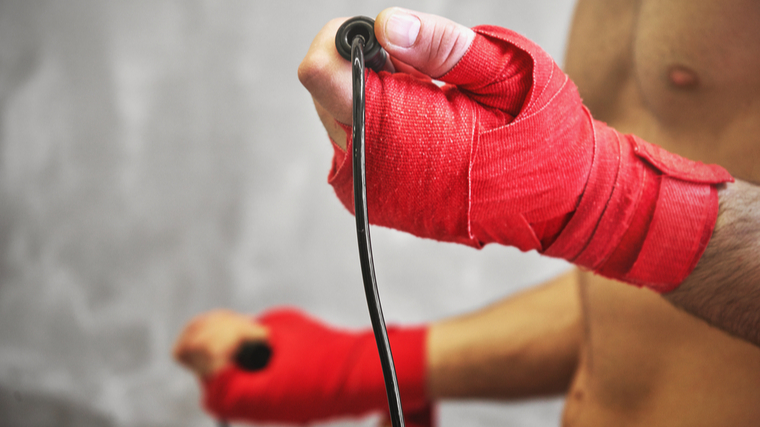 A person wears red wrist wraps and holds a jump rope up toward their bare chest.