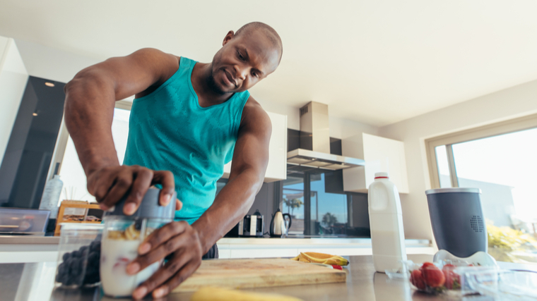 A person wears a green-blue tank top while making a smoothie in their kitchen.