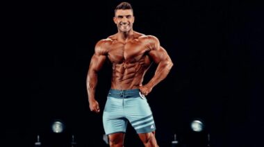 Ryan Terry wearin blue board shorts on a Men's Physique stage