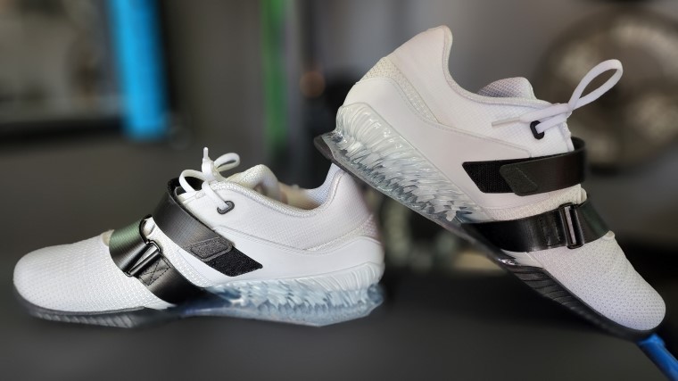 White and Black Nike Romaleos 4 weightlifting shoes sitting on a weight bench.