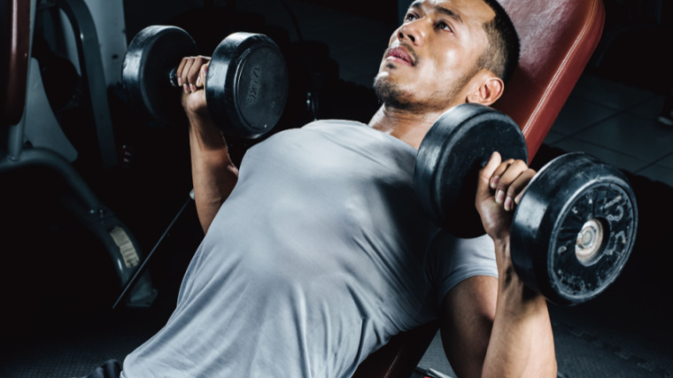 A person wearing a silver tank top prepares to perform an incline dumbbell bench press.