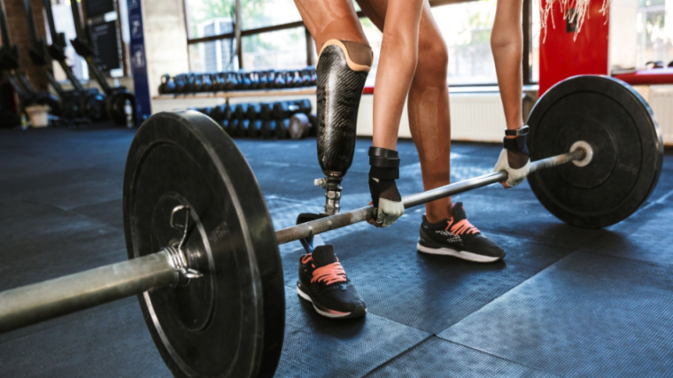 A person with a leg prosthesis prepares to perform a deadlift.