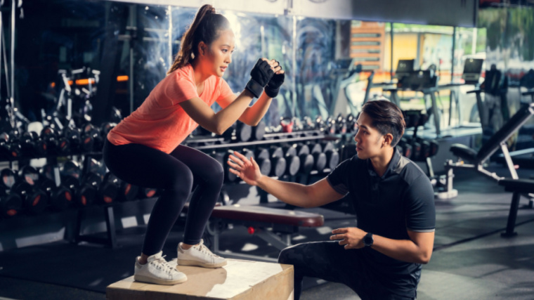 A person performs a box jump while their coach looks on.