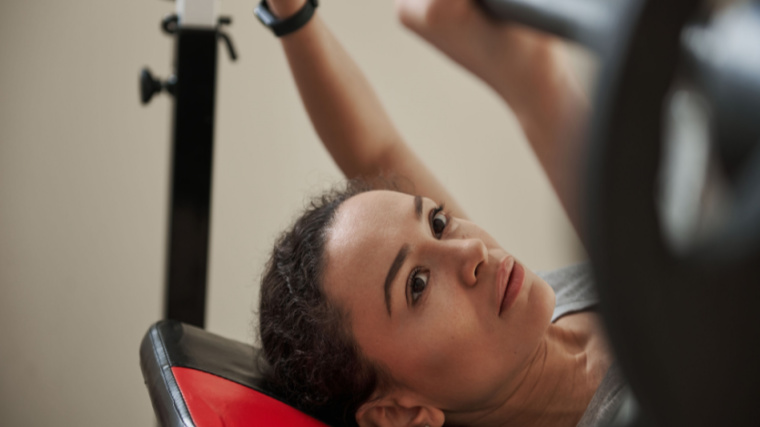 A person lies down to perform an incline bench press and looks up at the barbell.