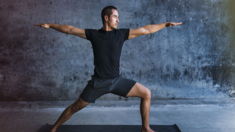 A person wears a black t-shirt while sinking into a warrior II pose.