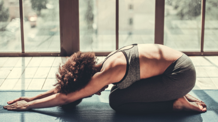 A person sinks into child's pose in a yoga studio with wall-to-wall windows.