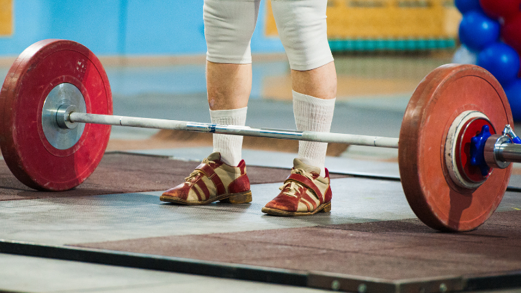 athlete stands before barbell in red weightlifting shoes