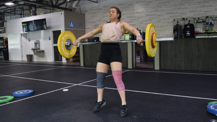 Weightlifter pulls barbell high during snatch exercise 