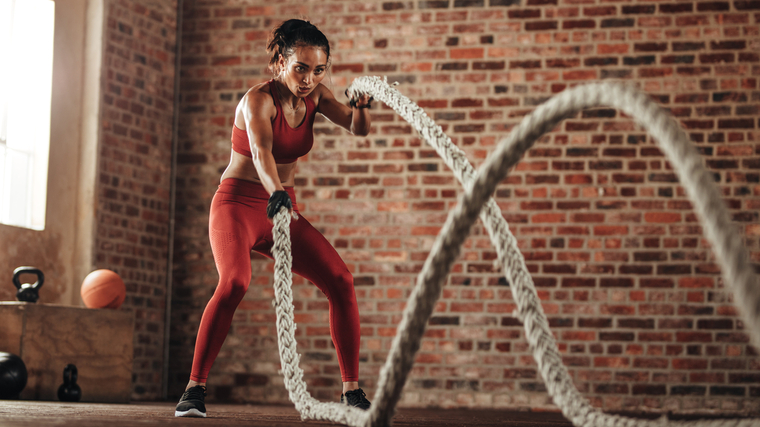 A person performs battle rope waves in a gym with brick walls.