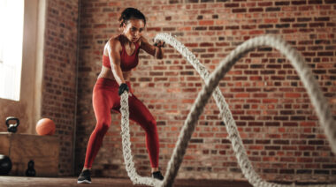 A person performs battle rope waves in a gym with brick walls.