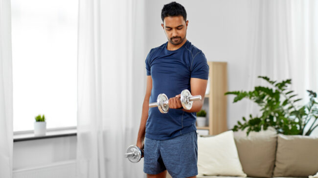 A person wearing a blue shirt performs a dumbbell curl at home.