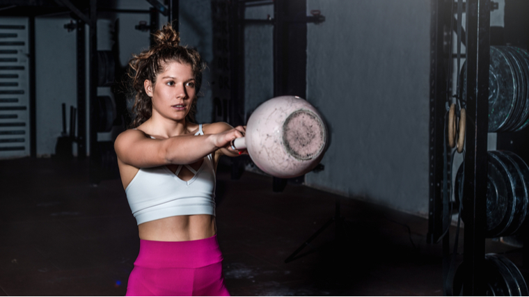 A person wearing a sports bra and bright pink leggings performs a kettlebell swing.