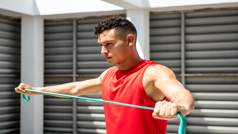 A person wearing a red tank top performs a band pull-apart.