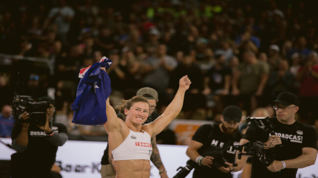 Tia-Clair Toomey holds up the Australian flag in one hand as she smiles at the crowd after winning the 2022 NOBULL CrossFit Games.