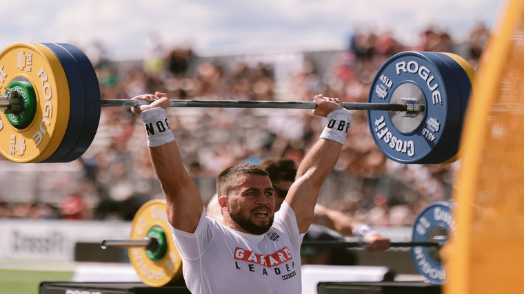 Ricky Garard wears a white leader jersey while holding a loaded bar over his head.