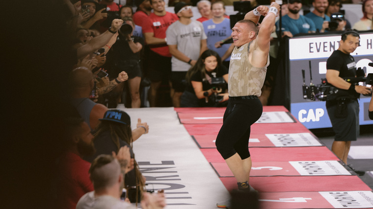 Roman Khrennikov celebrates an event finish with a smile and his arms raised above his head.