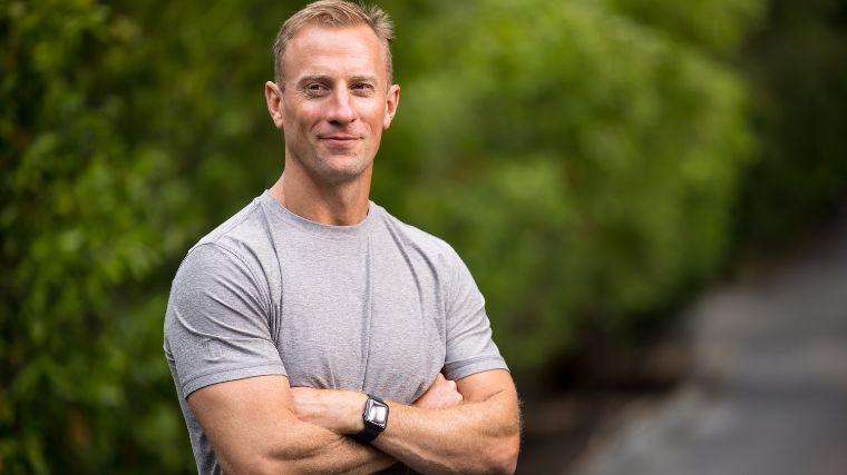 Man wearing a grey t-shirt folding his arms in front of green background