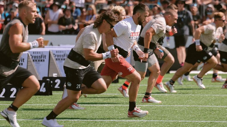 People wearing different colored t-shirts and shorts run outside on turf.