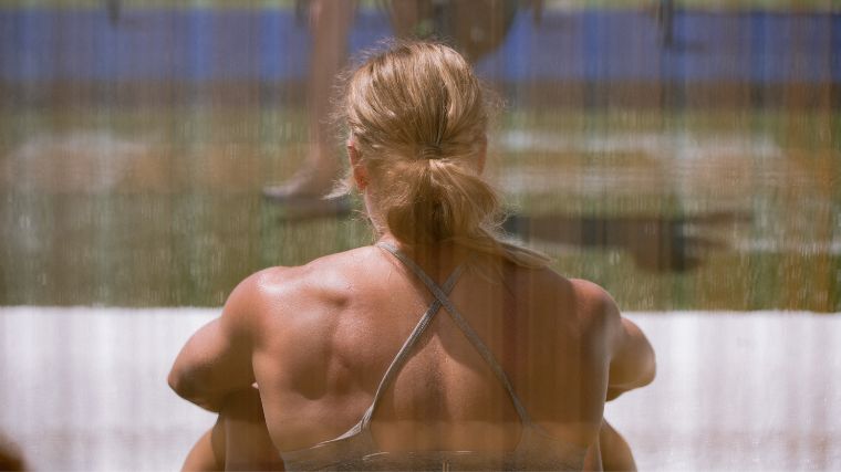 Brooke Wells sits with her back to the camera in front of an industrial fan to cool off after a Games event.