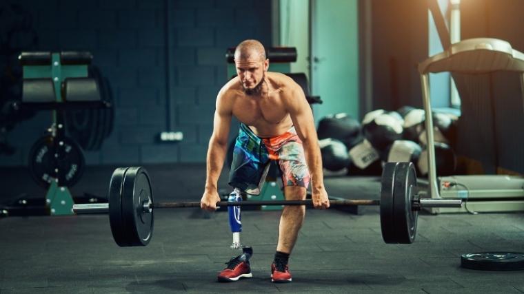 Person with a leg amputation wearing colorful shorts and no shirt deadlifting a loaded barbell