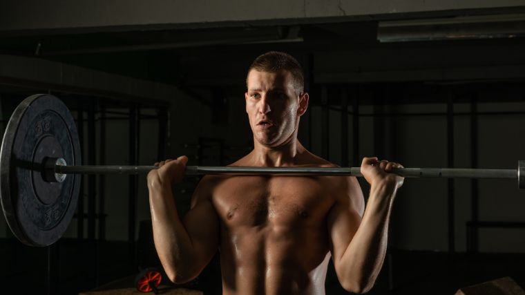 Shirtless person holding a loaded barbell across their chest.