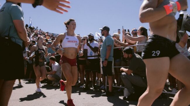 Tia-Clair Toomey wears the white leader jersey for the 2022 CrossFit Games as she jogs out onto the competition floor past the crowd.