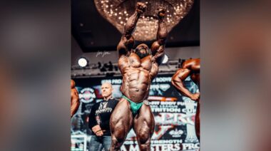 Akim Williams on stage, wearing blue posing trunks, after winning the 2022 Tampa Pro.