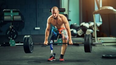 Person with a leg amputation wearing colorful shorts and no shirt deadlifting a loaded barbell