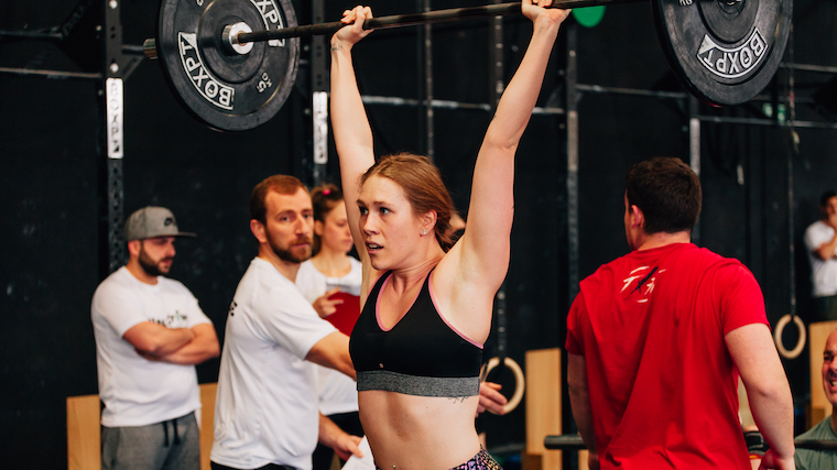 Woman strength athlete performing thruster over head in competition