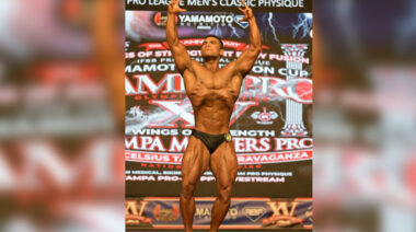 A shirtless bodybuilder posing with his hands stretched to the sky.