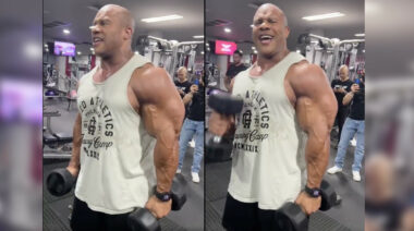 Bodybuilder Phil Heath doing curls in a sleeveless shirt at the gym.