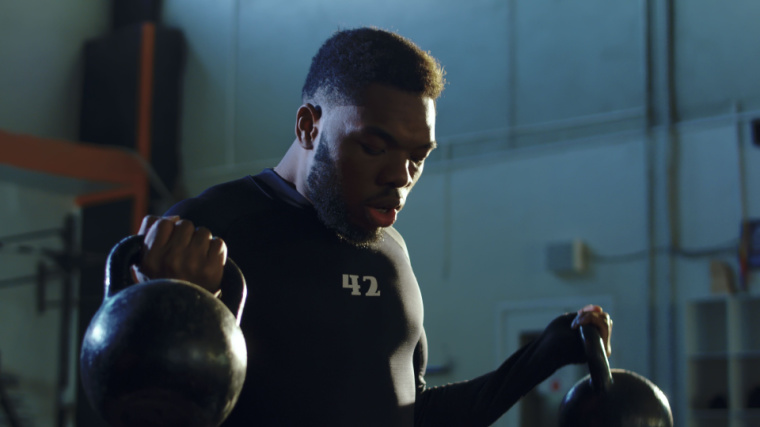 A person wears a black t-shirt with the number 42 on the chest while performing double kettlebell biceps curls.